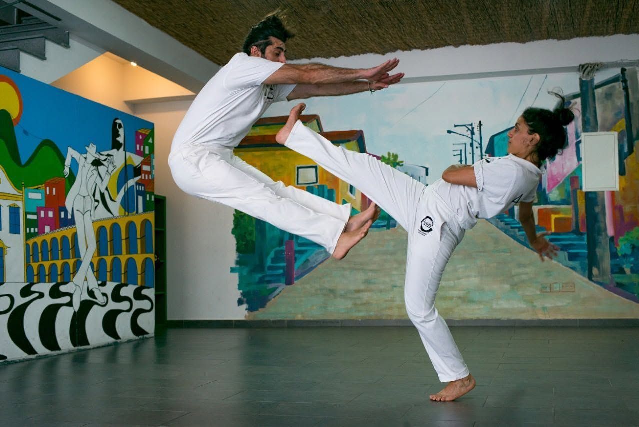 Two Apêiara capoeiristas playing at the academy, one jumping over a high kick